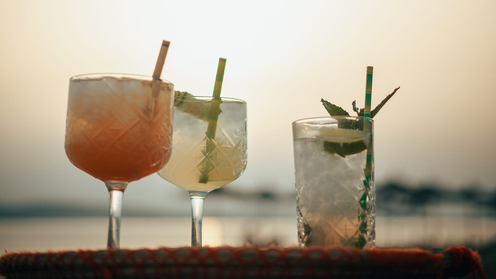 Three cocktails on a tray against the Aegean at sunset