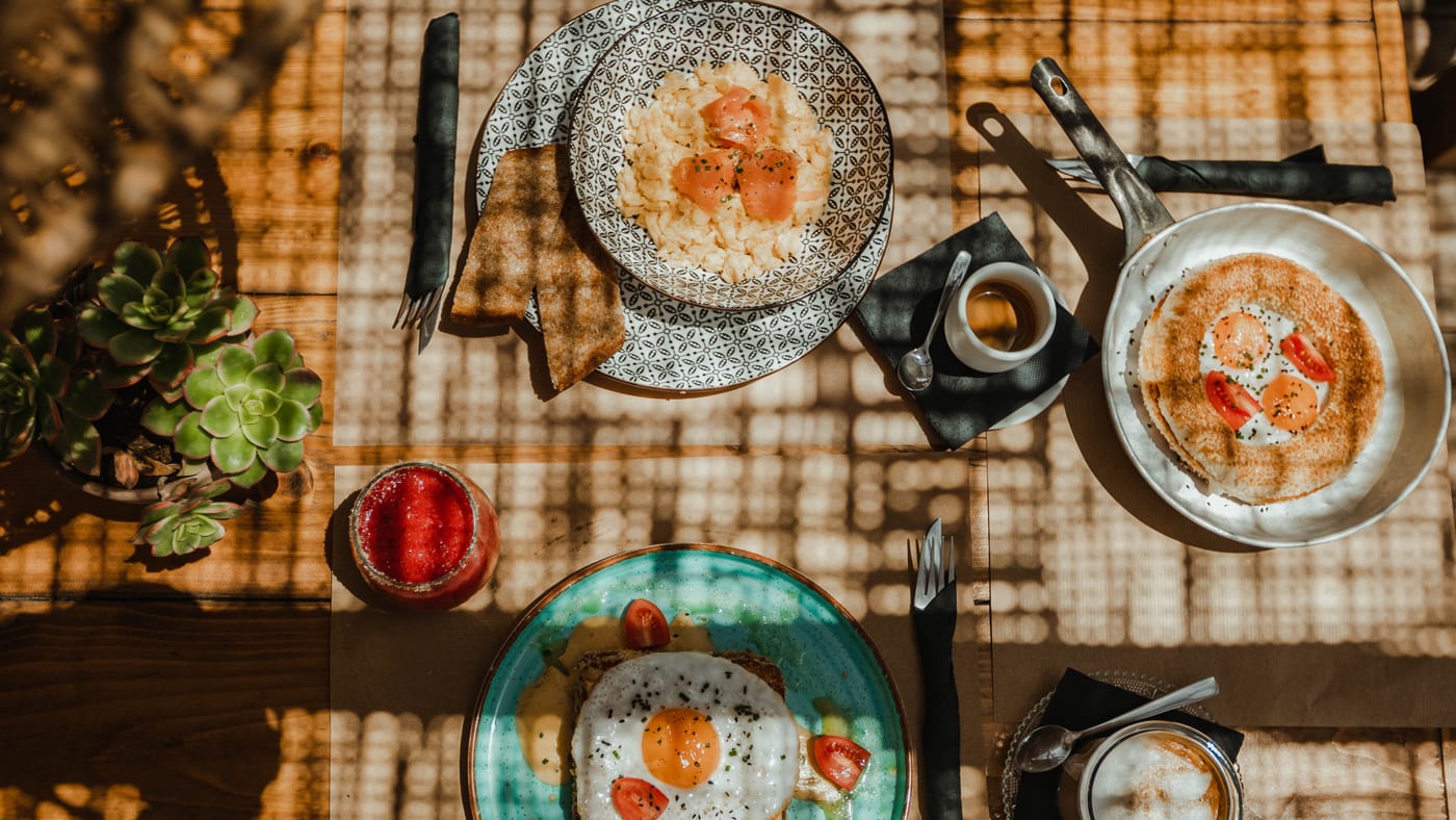 A breakfast spread from above — eggs, plates and coffee under the reed shade