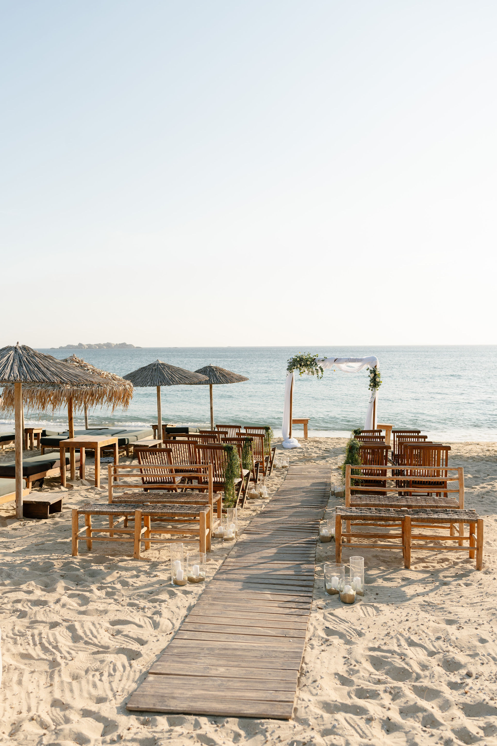 The beach set for a ceremony — benches, candles and a wooden walkway to the sea