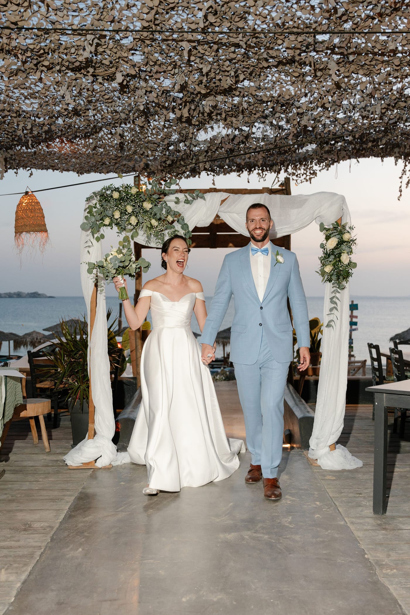 The newlyweds hand in hand beneath the arch at dusk