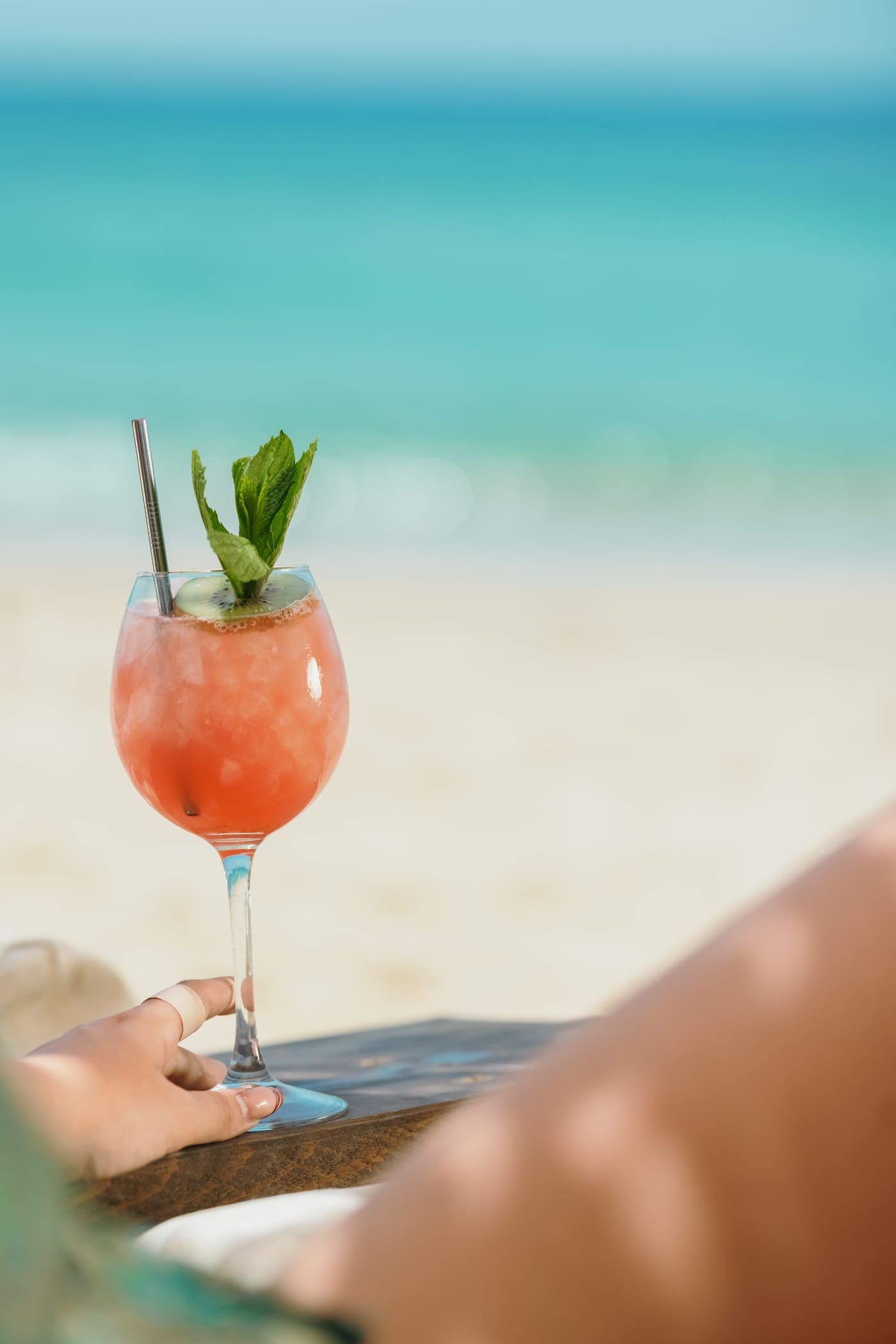 A pink cocktail held against the turquoise sea