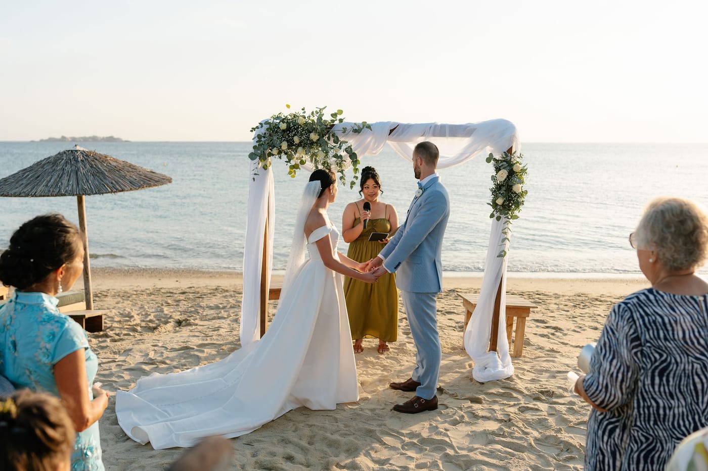 A beach wedding ceremony beneath a floral arch