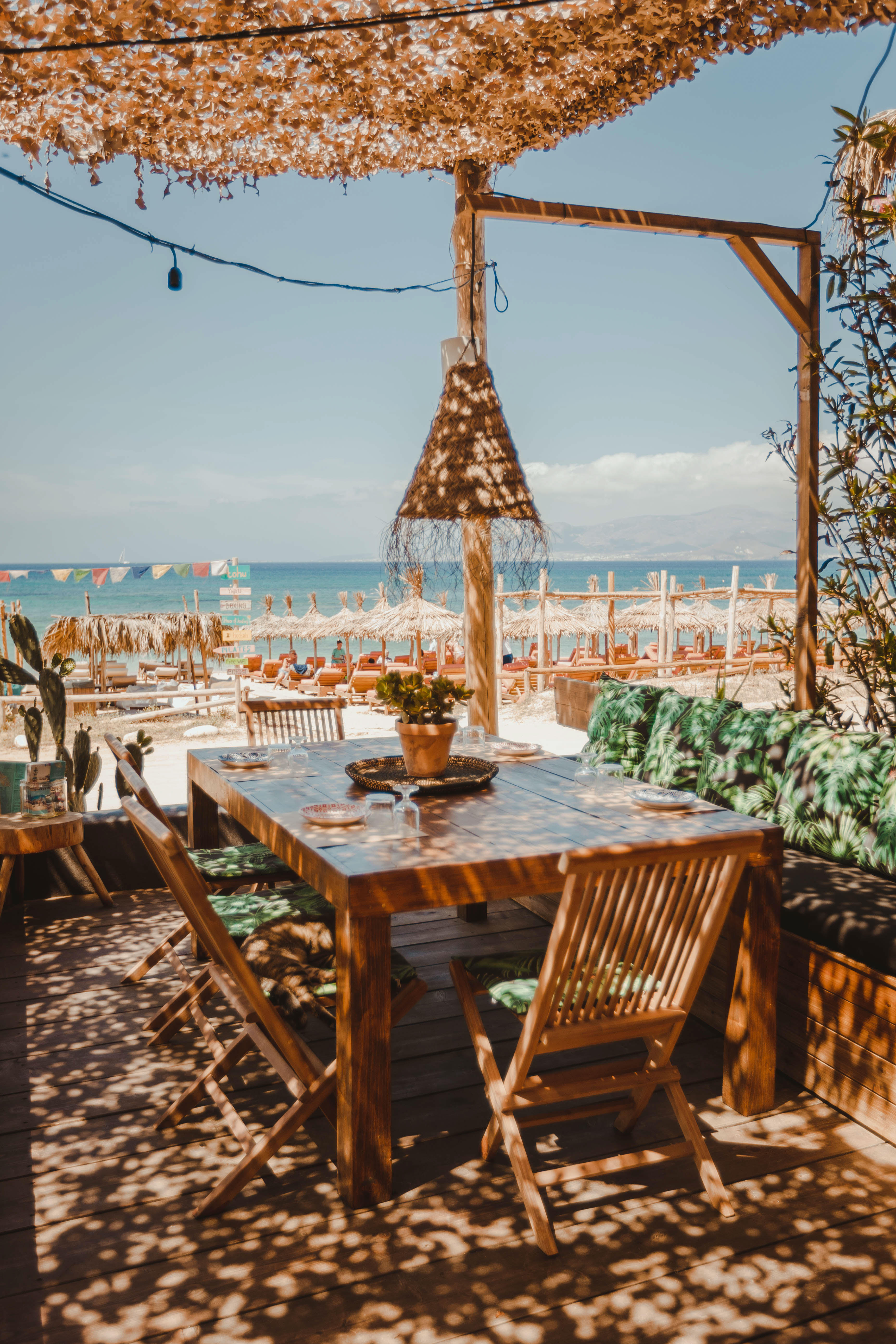 A dining table on the deck under the reed canopy looking out to umbrellas and the sea