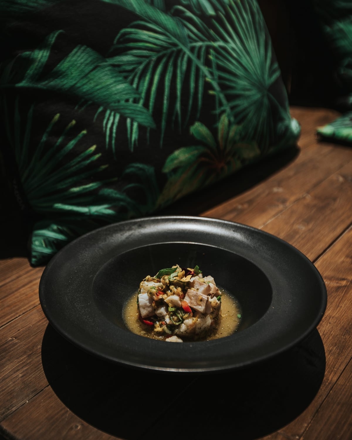 Sea bass ceviche in a black bowl beside tropical-print cushions
